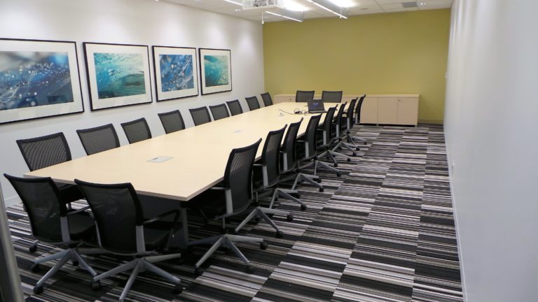 A long conference table surrounded by chairs with artwork on a single wall