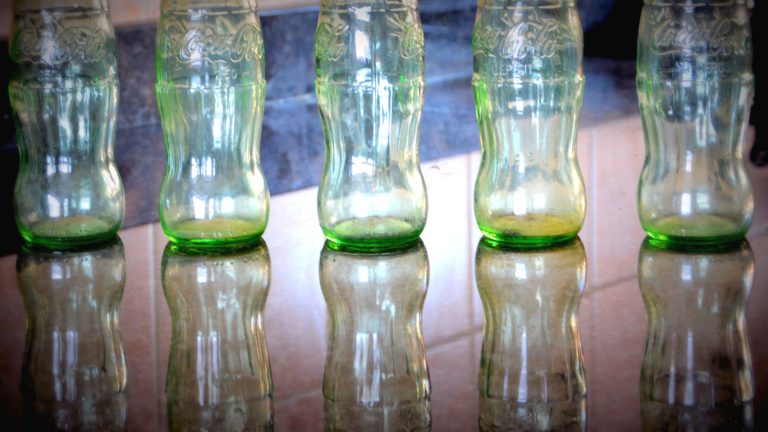 3 glass Coca Cola bottles lined up on a table.