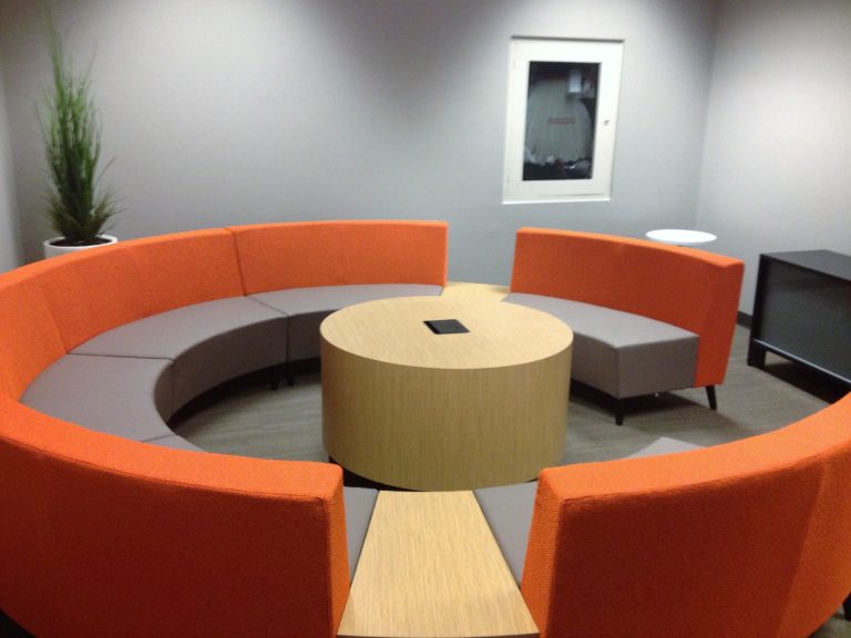A round grey and orange sectional seating arrangement with a circular table in the centre