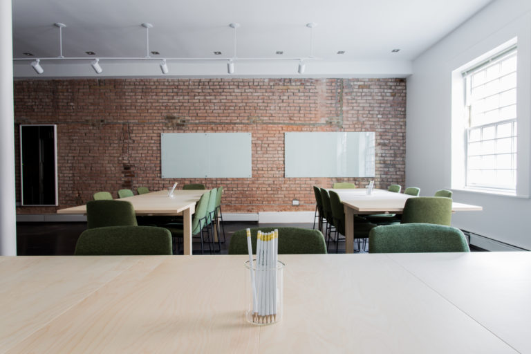 An office with two long tables facing an exposed brick wall with 2 whiteboards