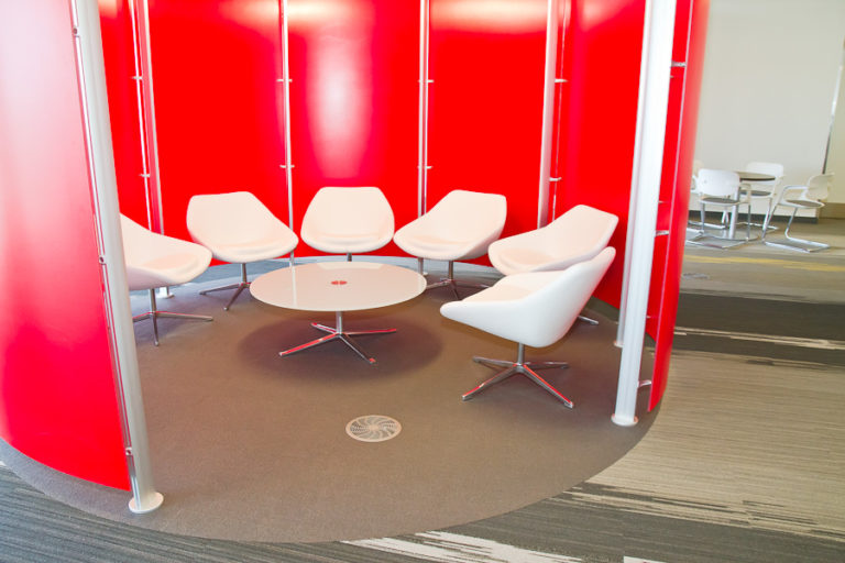 A red semi-circular room with a row of white chairs and a round coffee table