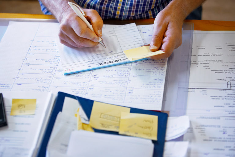A person writing noted on a desk covered in papers and post-its