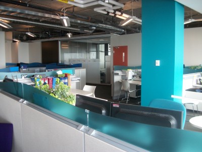 An office space with bright teal walls and decorated cubicles.